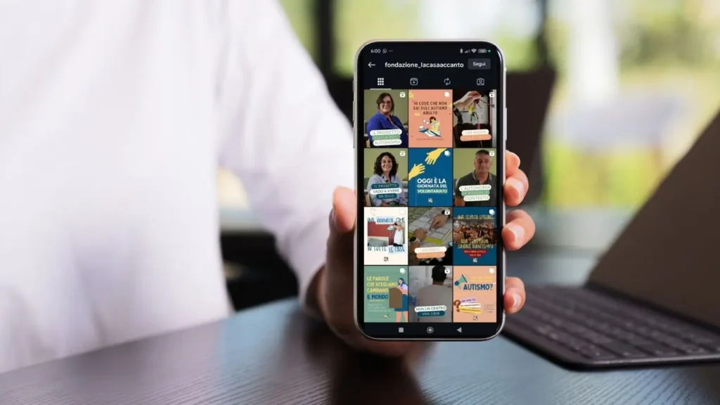 una persona regge il telefono in cui si vede il feed instagram della casa accanto pieno di post social informativi sull'autismo